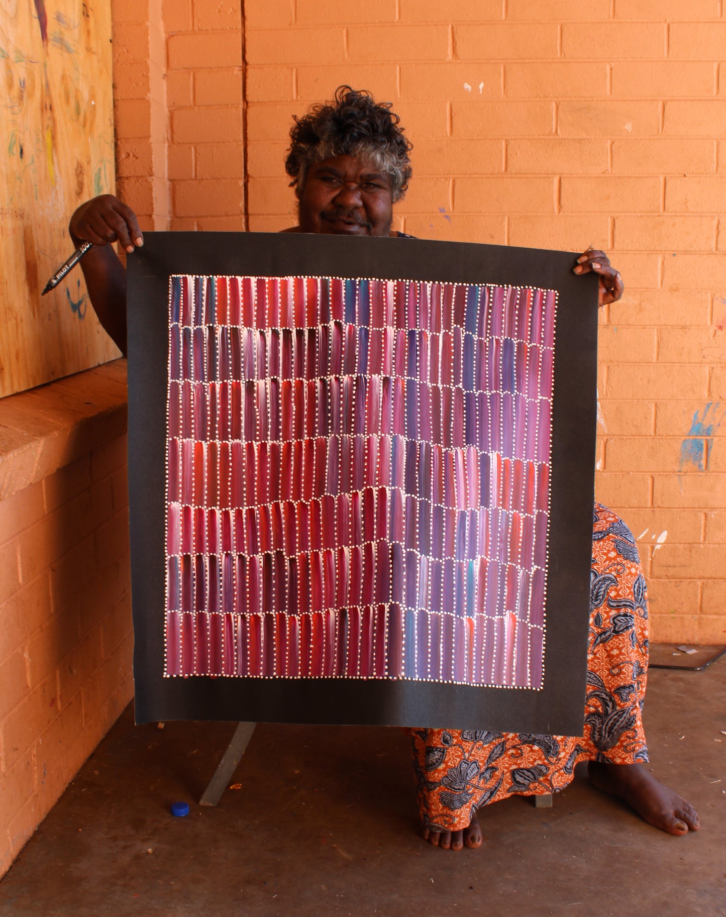 Jeannie Mills Pwerle holding her painting representing the anaty or bush yam.