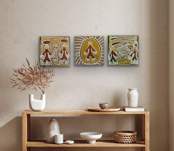 Three Linda Syddick Napaltjarri paintings on a wall above a wooden console table with decorative items.