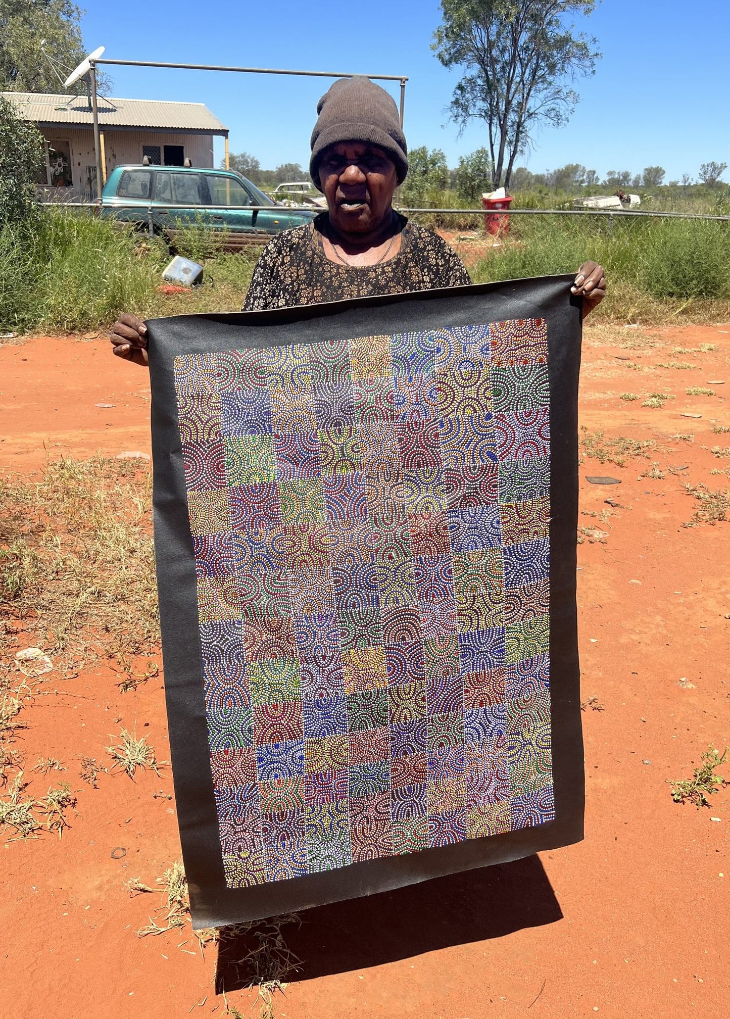 Artist Lizzie Moss Pwerle holding her colourful 90x60cm painting.