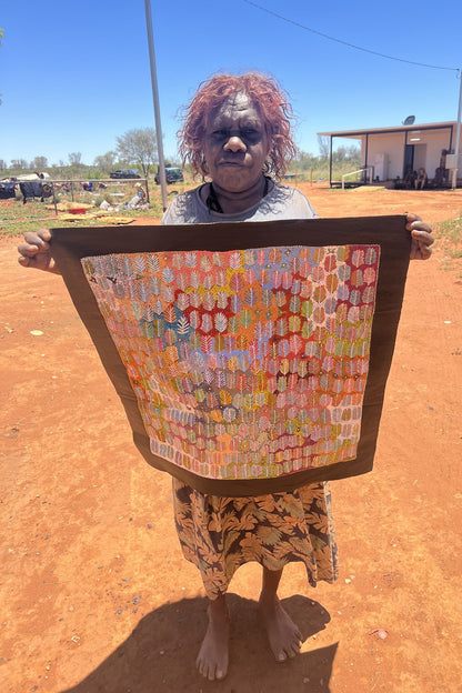 Artist Betty Morton holding her painting with a pattern of leaf-like shapes in a variety of colours.