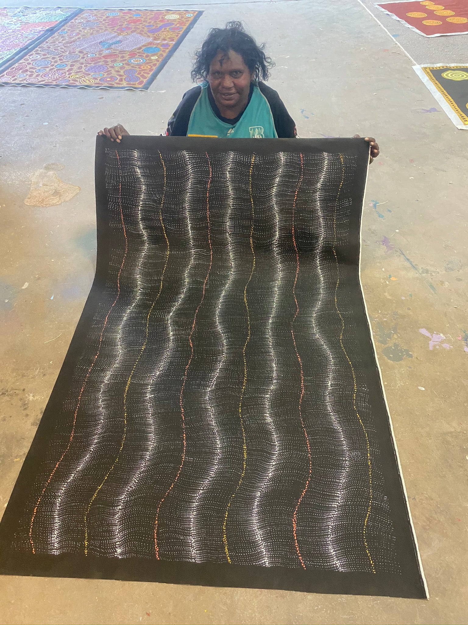 Debbie Brown Napaljarri holding her 'Bush Tomato Dreaming (Wanakiji Jukurrpa)' painting 95x150cm Unstretched White Orange Yellow