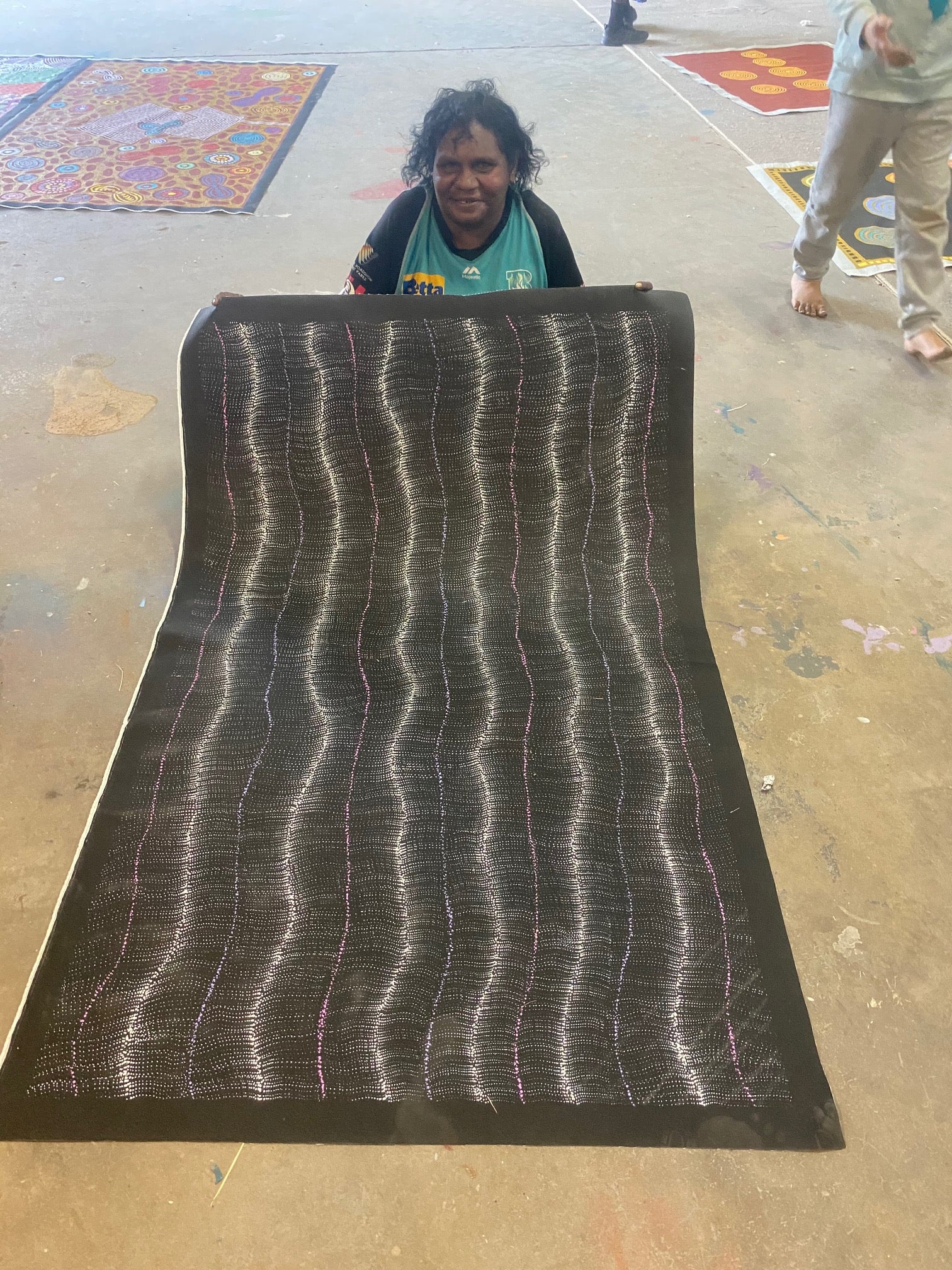 Debbie Brown Napaljarri holding her 'Bush Tomato Dreaming (Wanakiji Jukurrpa)' painting 95x150cm Unstretched White Pink Purple