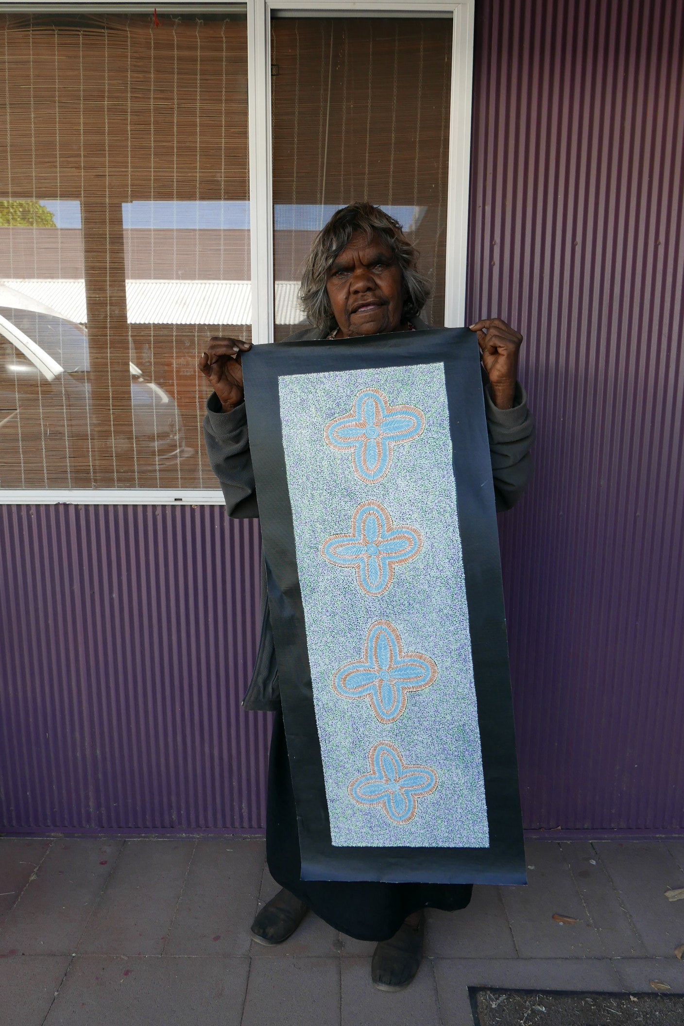 Audrey Morton Kngwarreye holding her Ilyarnayt Flower painting 89x30cm