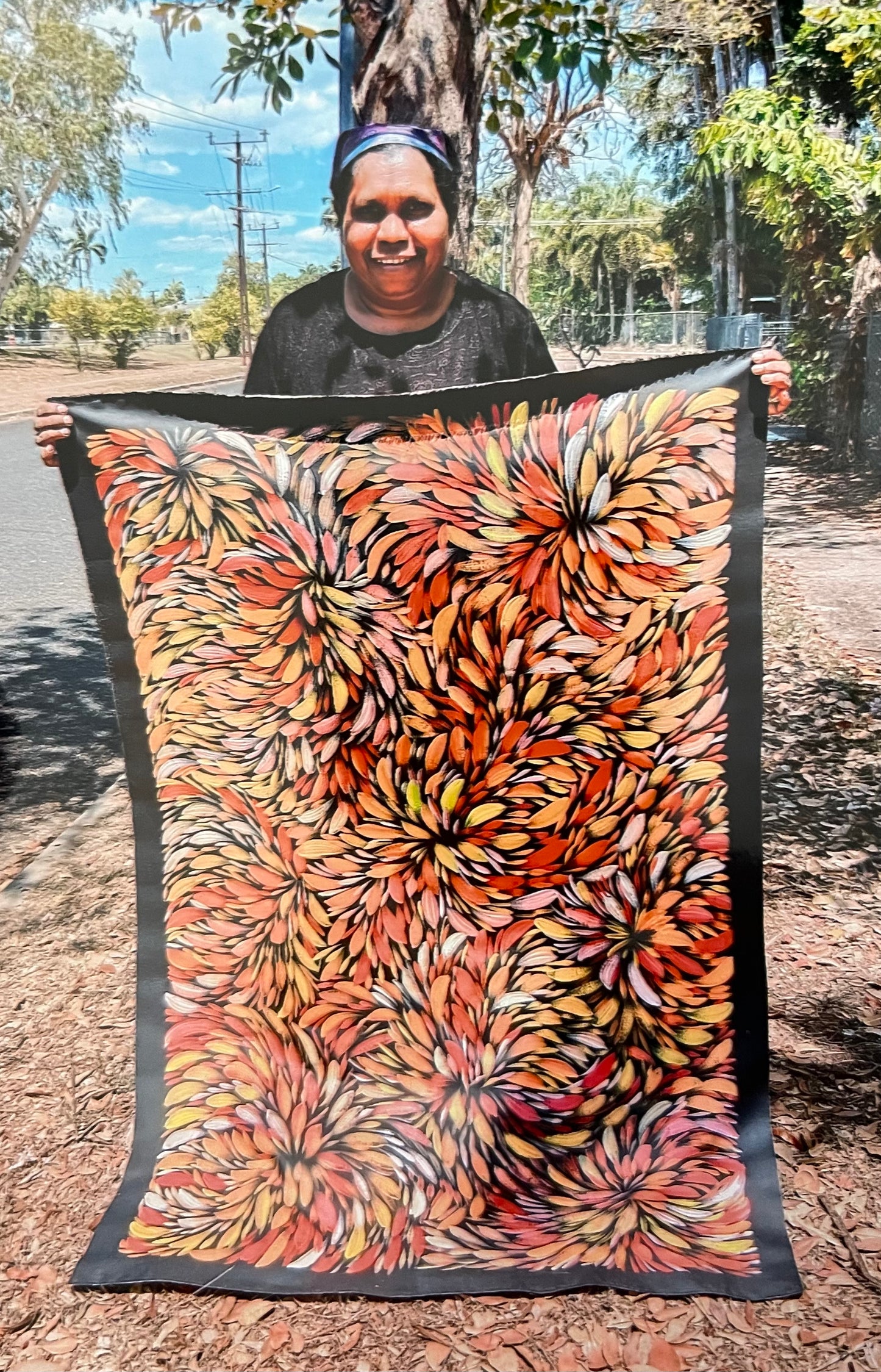 Selina Numina Kamprina holding her vibrant bush medicine leaves painting with floral-leave like motifs in red, orange, yellow and white.