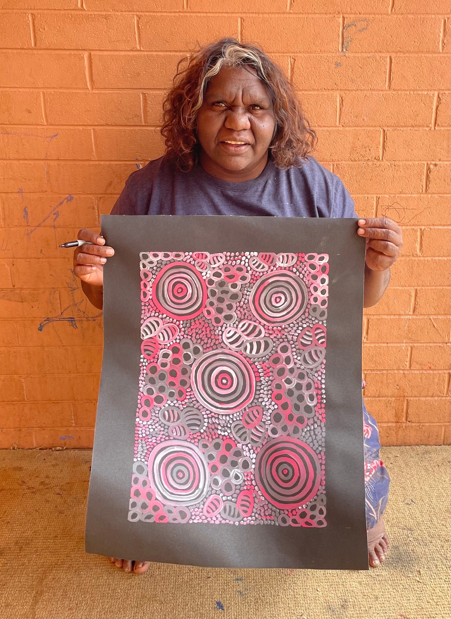 Dulcie Long Pula holding her 'Awelye-Atnwengerrp (Body Paint)' painting 51x36cm Pink Grey White