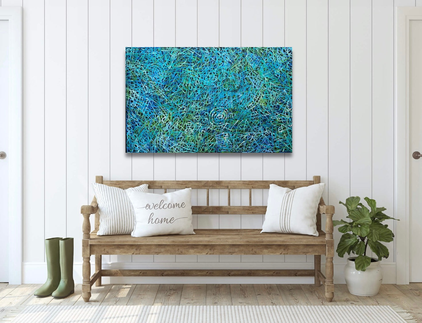 An awelye painting by Betty Club Mbitjana in blue, green, aqua and white colours hanging on a wall above a wooden bench seat.