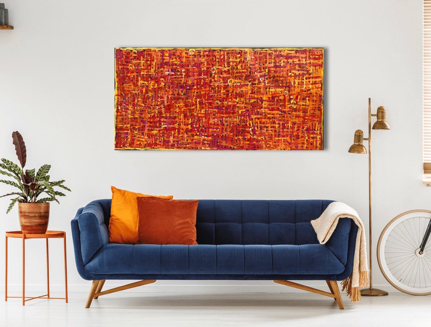 A painting by Betty Club Mbitjana hanging on a wall above a blue couch, coffee table and lamp.