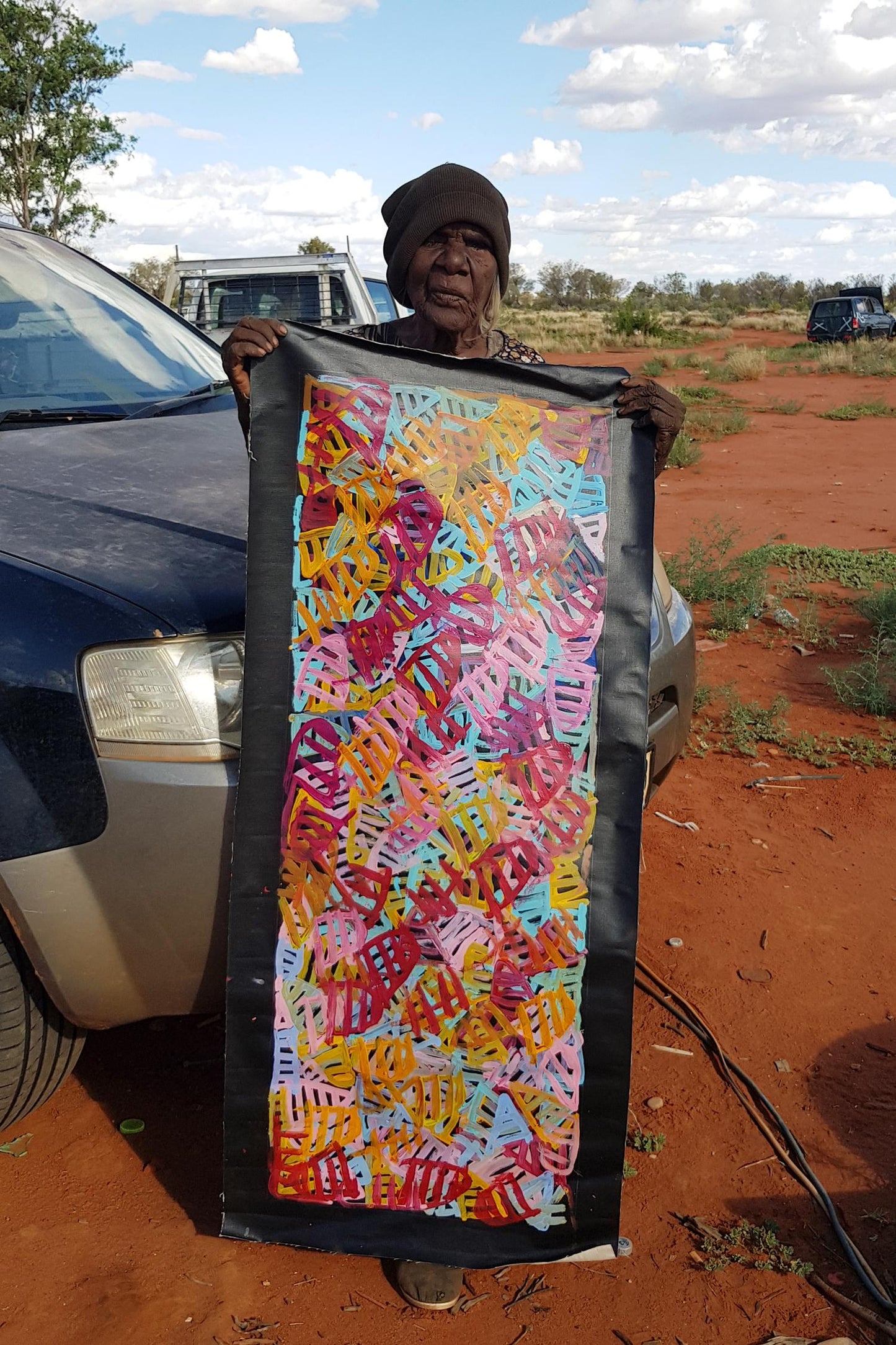 Emily Pwerle holding her 'Awelye (Women's Ceremony)' painting, 120x45cm