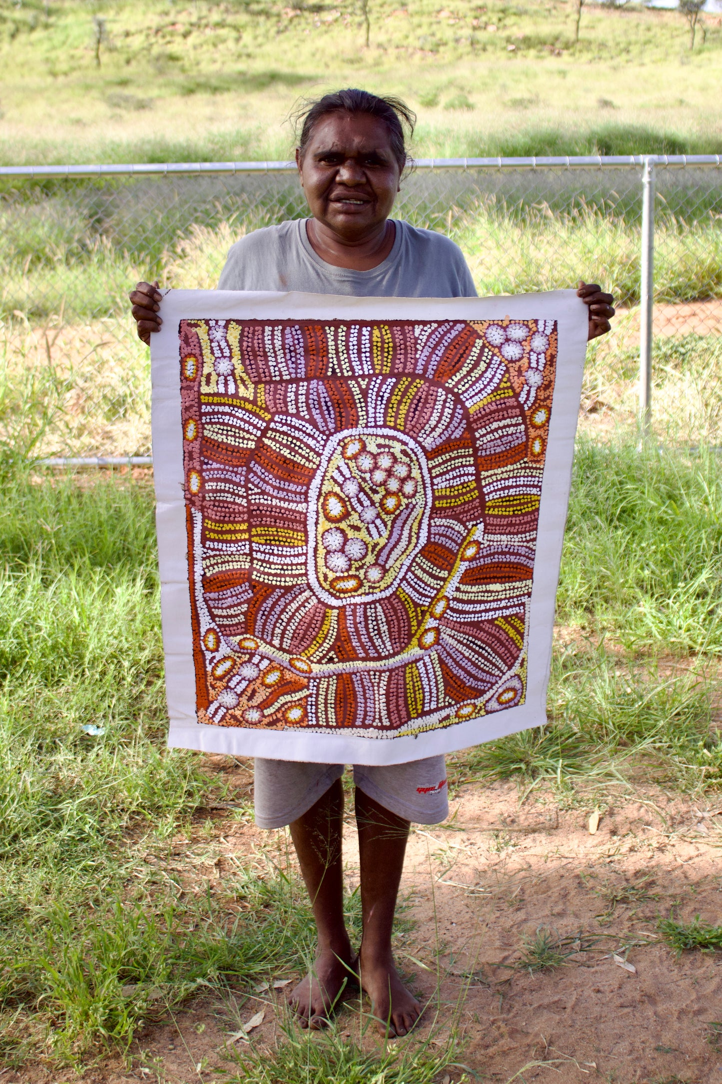 Esther Bruno Nangala holding her 'Marrapinti - Bush Raisin' painting 60x60cm