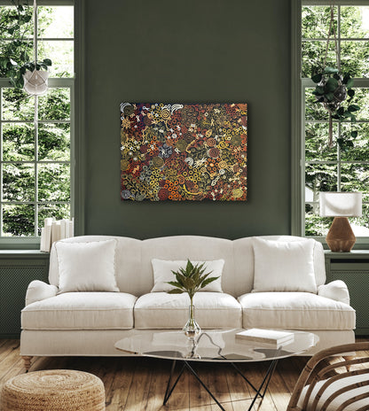 A painting by Meredith Curley hanging on a green wall above a modern white sofa, the painting features swirling patterns and symbols (a depiction of women collecting bush foods) with a predominantly brown, black, red, orange, and yellow colour palette.
