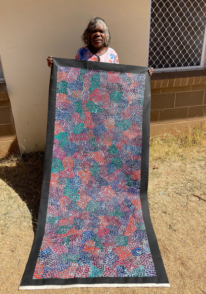 Eileen Bird Kngwarreye holding her 'Arlatyeye (Pencil Yam) Dreaming' painting 80x183cm Multi
