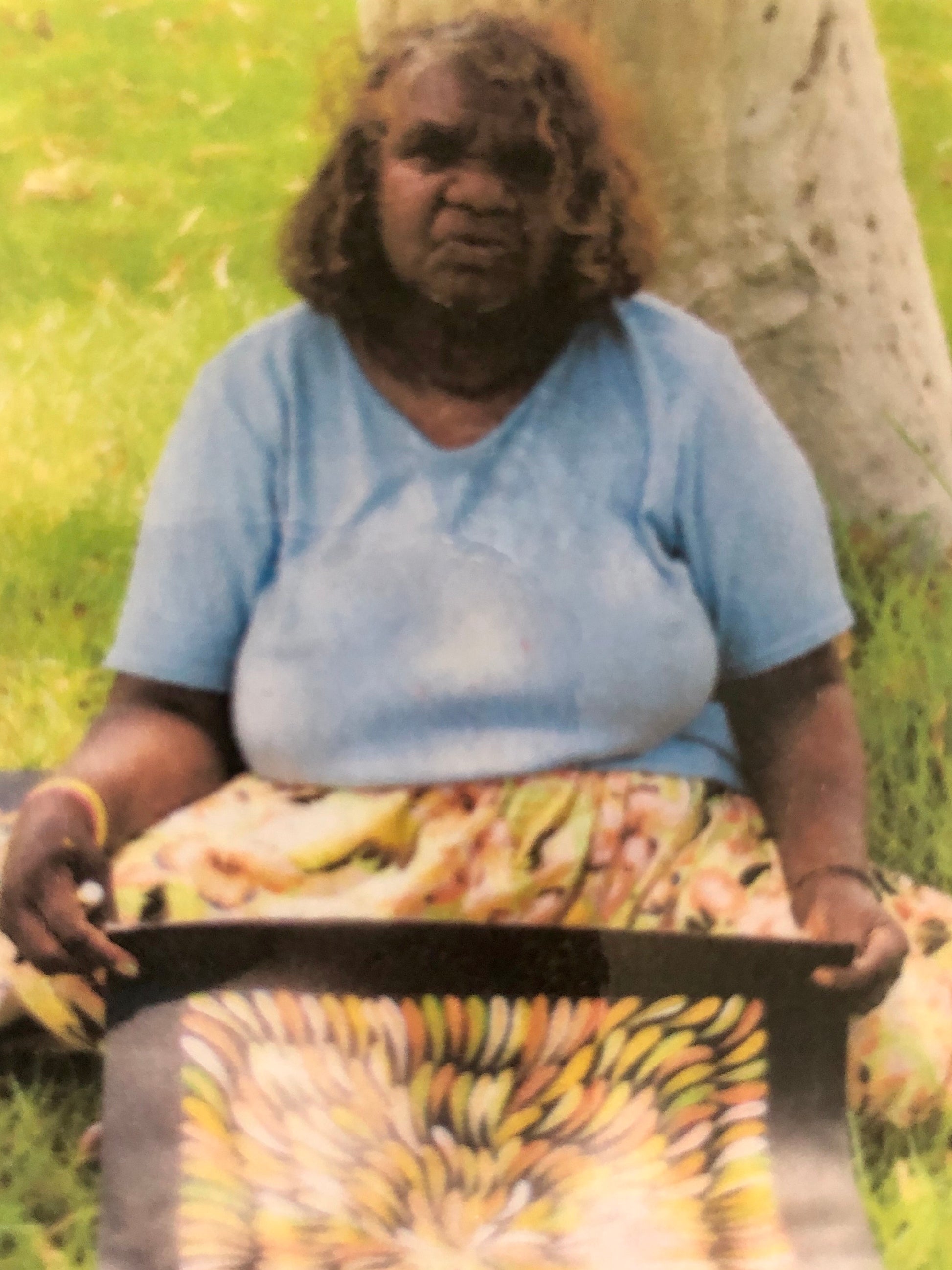 Mary Rumble holding her bush medicine leaves painting featuring a vibrant, pattern of intertwined medicine leaves in various warm fawn, orange and white colours.