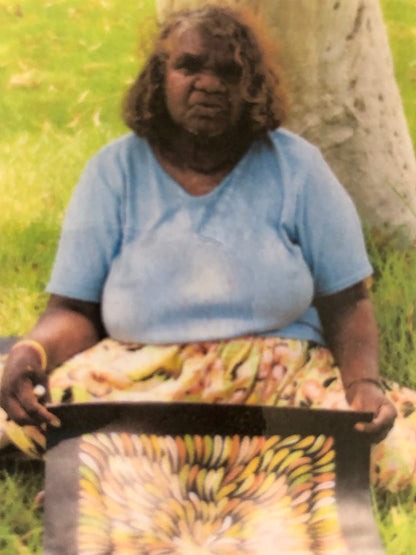 Mary Rumble holding her bush medicine leaves painting featuring a vibrant, pattern of intertwined medicine leaves in various warm fawn, orange and white colours.