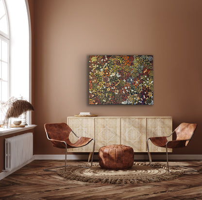 A painting by Meredith Curley hanging on a brown wall above a modern side table and brown leather chairs, the painting features swirling patterns and symbols (a depiction of women collecting bush foods) with a predominantly brown, black, red, orange, and yellow colour palette.