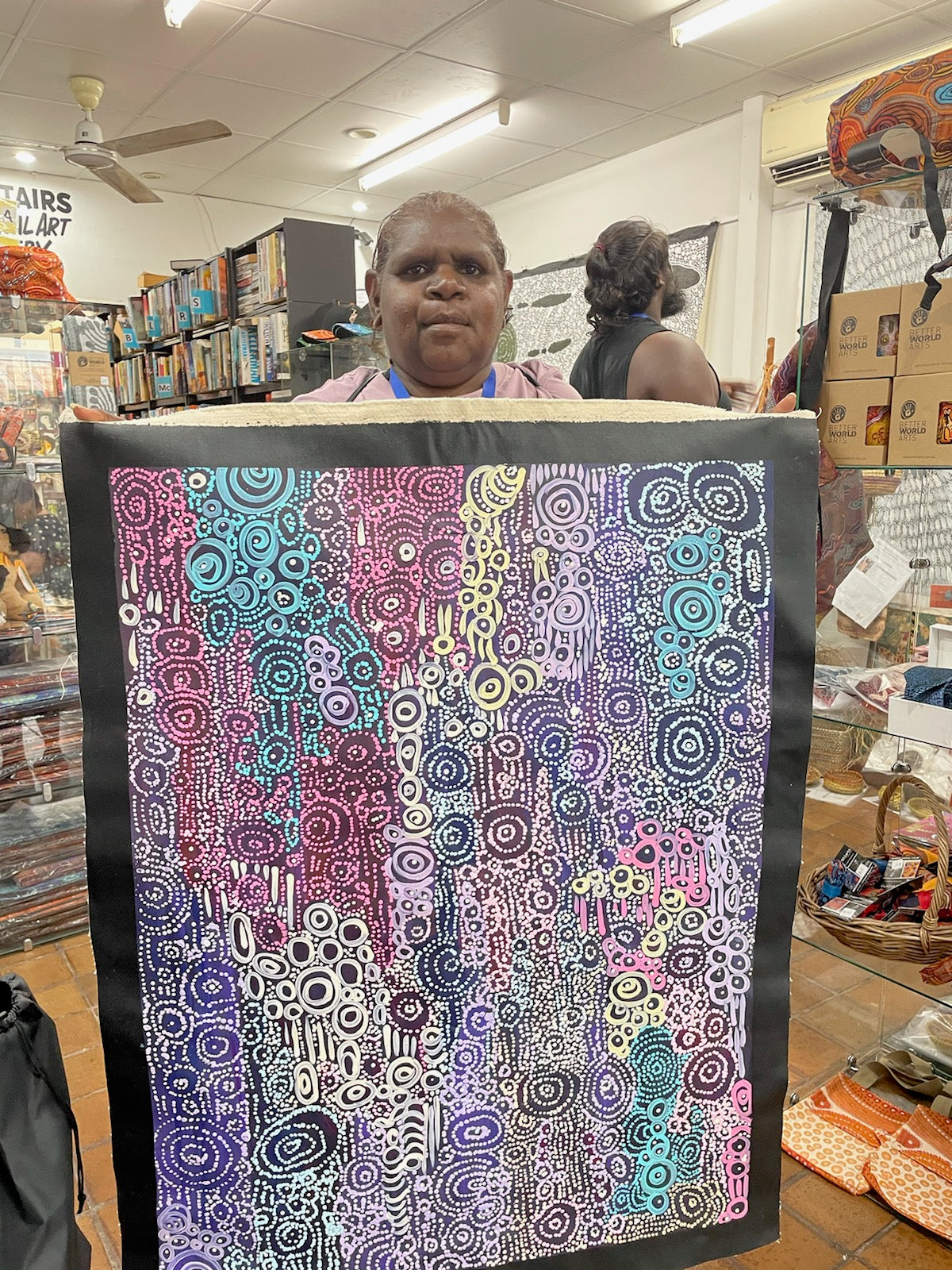 Meredith Curley holding her painting featuring a pattern of swirling circles in various shades of blue, purple, and white on a black background.