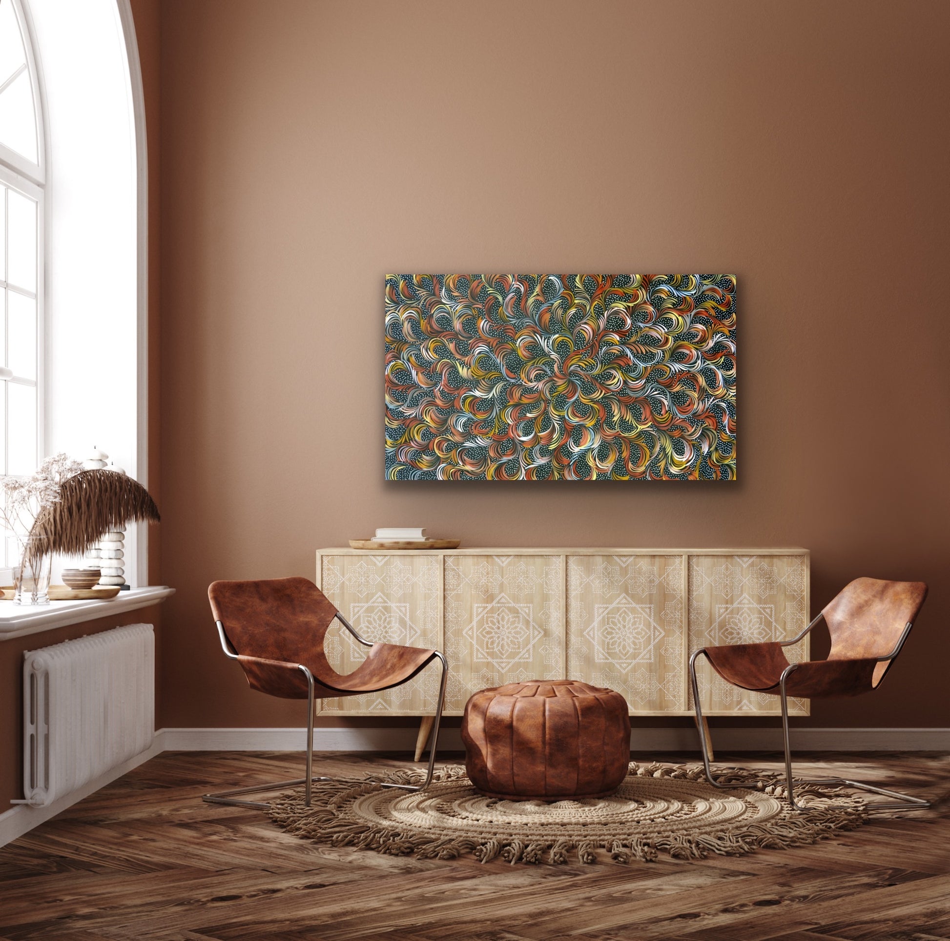 A painting by Selina Numina Kamprina hanging above a light brown wooden console with modern leather chairs and other décor items.