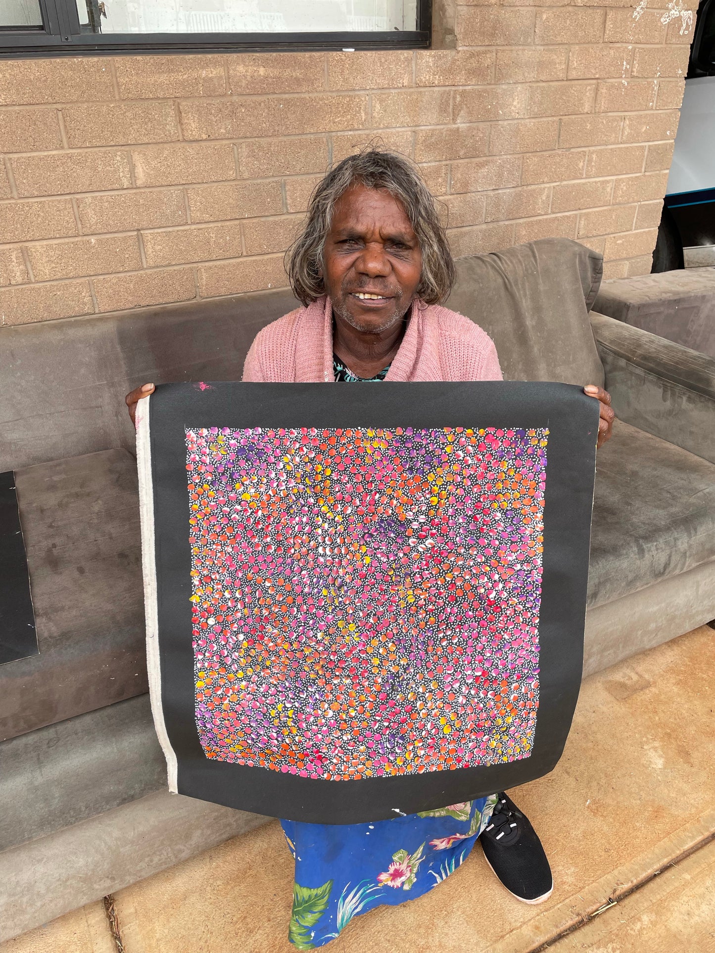 Eileen Bird Kngwarreye holding her 'Arlatyeye (Pencil Yam) Dreaming' painting 45x45cm Multi