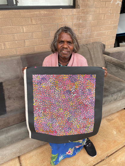Eileen Bird Kngwarreye holding her 'Arlatyeye (Pencil Yam) Dreaming' painting 45x45cm Multi