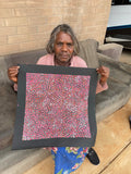 Eileen Bird Kngwarreye holding her 'Arlatyeye (Pencil Yam) Dreaming' painting 45x45cm Multi