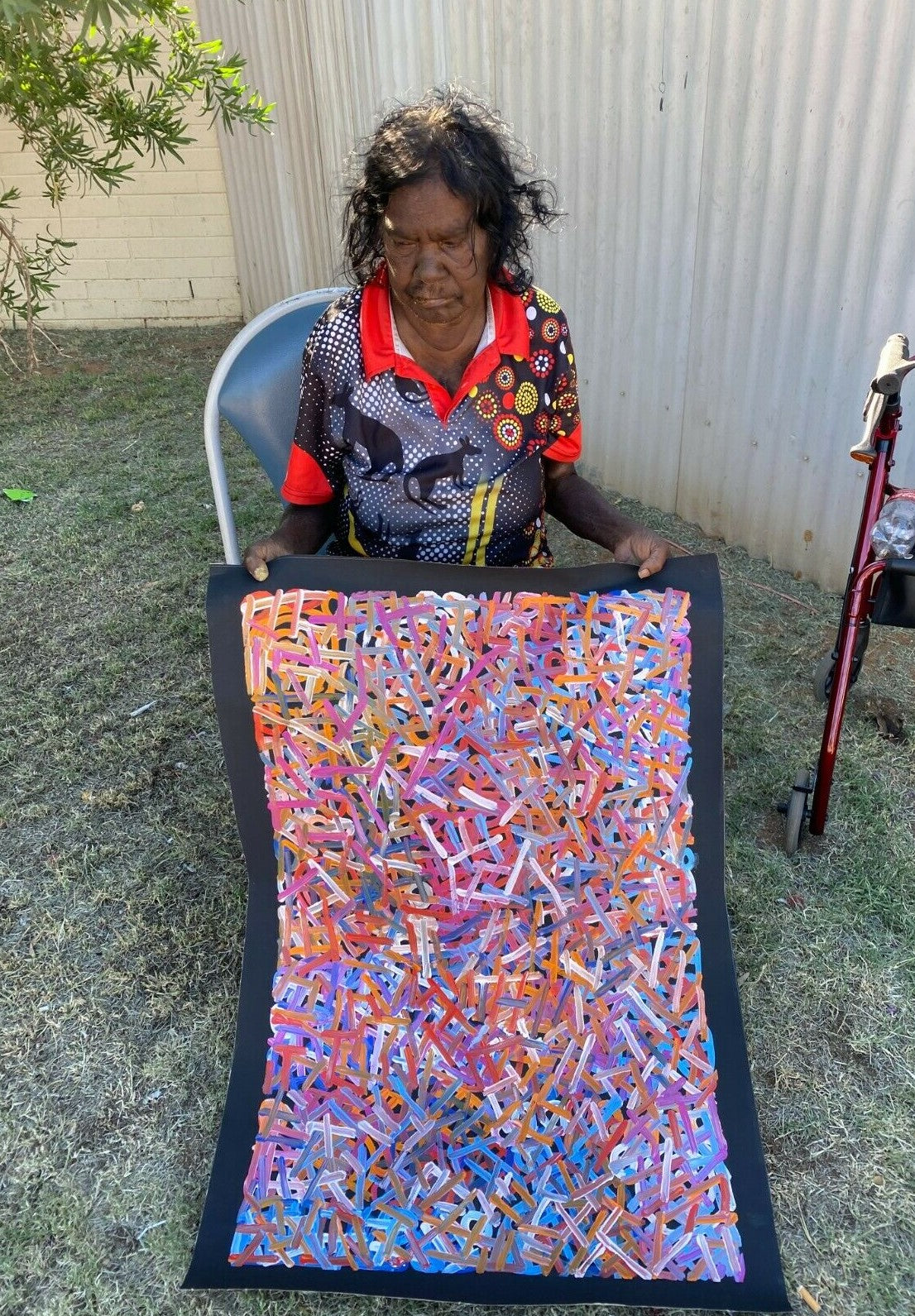 Betty Club Mbitjana holding one of her vibrant multicoloured 90x60cm paintings.