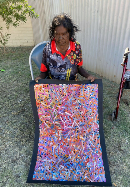 Betty Club Mbitjana holding one of her vibrant multicoloured 90x60cm paintings.
