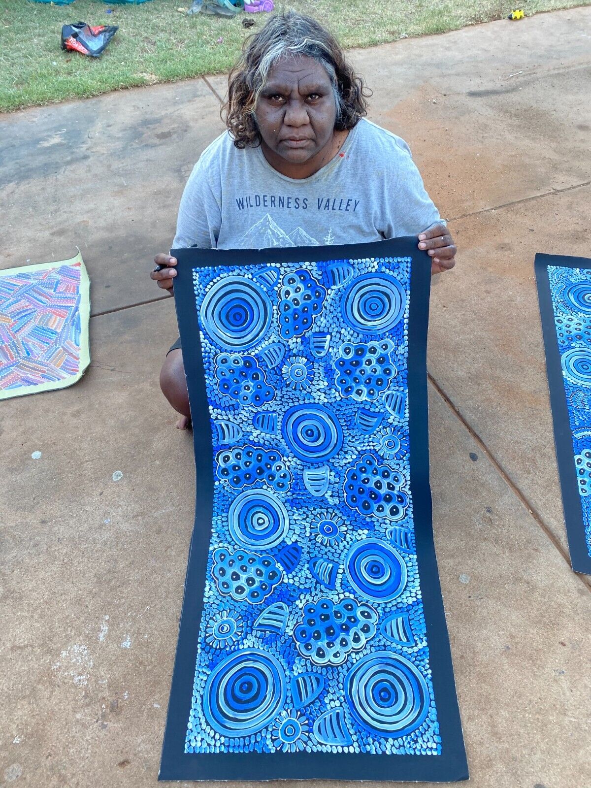 Dulcie Long Pula holding her 'Awelye-Atnwengerrp (Body Paint)' painting 102x44cm Blues White